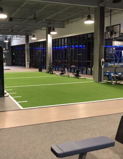 Indoor athletic facility featuring performance turf for training, equipped with fitness machines and illuminated by blue lighting, emphasizing high-intensity training zones.