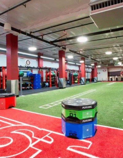Gym interior featuring turf flooring, stacked training equipment, and designated workout zones, emphasizing customized flooring solutions for functional fitness and dynamic movement training.