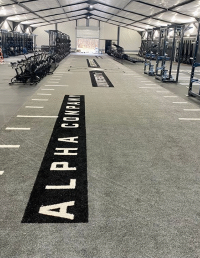 Athletic training facility featuring high-quality performance turf with "ALPHA COMPANY" branding, designed for sled work and agility drills, emphasizing durability and safety in training environments.