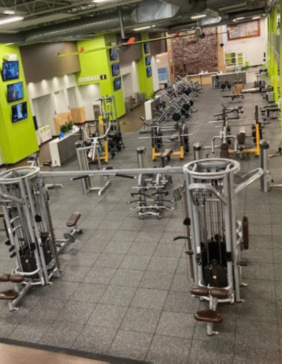 Gym interior showcasing various workout machines and rubber flooring, designed for weight training and cardio, emphasizing safety and performance in fitness zones.