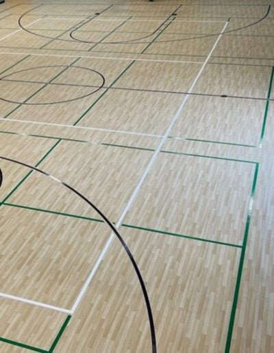 Basketball court flooring featuring polished wood finish, clear court markings, and vibrant green lines, illustrating high-quality refinishing by Sport Pro Surfacing.