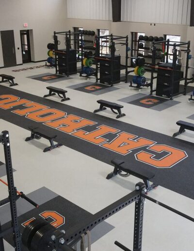 Weight room featuring high-performance rubber flooring with custom "C" logo, weightlifting equipment, and benches, designed for safety and team identity.