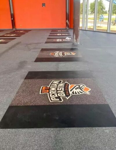 Rubber flooring in a weight room featuring custom logos for the UTPB Falcons, showcasing a vibrant design and enhancing team identity.