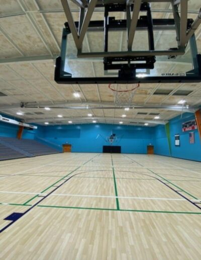 Basketball court with polished hardwood flooring, bright blue walls, and overhead hoop, showcasing refinished sports flooring at Greenwich YMCA.