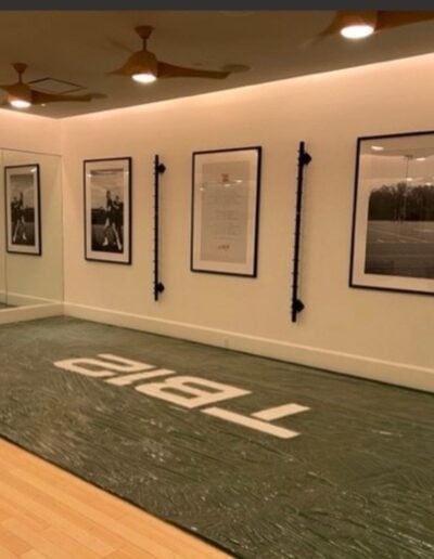 Indoor facility featuring a green turf area with "TABI" branding, framed sports photographs on the walls, and a sleek, modern design emphasizing seamless transitions for high-traffic entryway solutions.