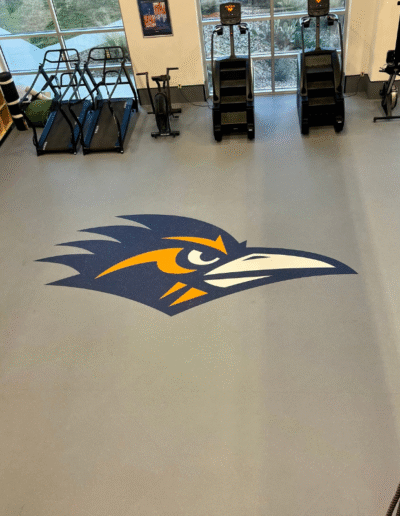 Logo of a stylized bird in blue and orange on a sports flooring surface, showcasing custom branding for athletic facilities.