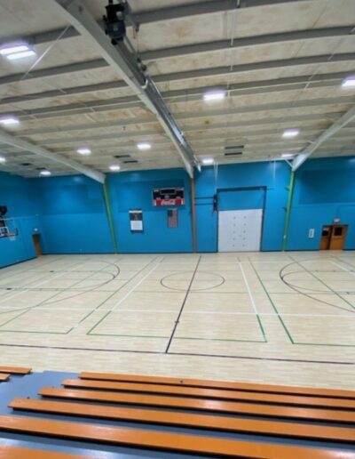 Basketball court with polished hardwood flooring, teal walls, and bleachers, showcasing a well-maintained sports facility by Sport Pro Surfacing.