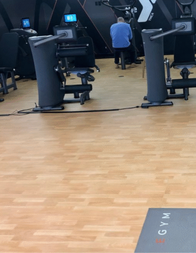 Gym interior showcasing wood-patterned flooring, fitness equipment, and a person exercising, illustrating customized gym flooring solutions by Sport Pro Surfacing.