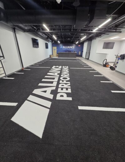 Indoor athletic facility featuring black turf with "ALLIANCE PERFORMANCE" branding, designed for high-intensity training and functional movements.