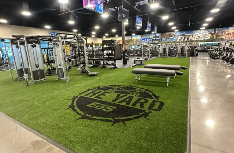 Gym interior featuring artificial turf flooring with "THE YARD" logo, fitness equipment, and workout benches, illustrating commercial flooring benefits in health clubs.