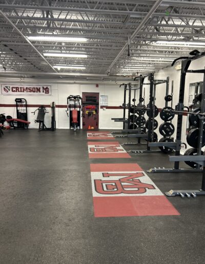 Weight room featuring high-performance rubber flooring with custom logos, strength training equipment, and a bright, energizing environment emphasizing school pride and safety.