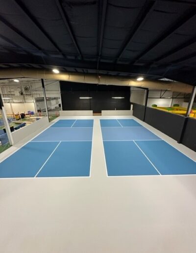 Indoor sports facility featuring newly resurfaced tennis and pickleball courts with blue playing surfaces and white lines, designed for optimal performance and durability.