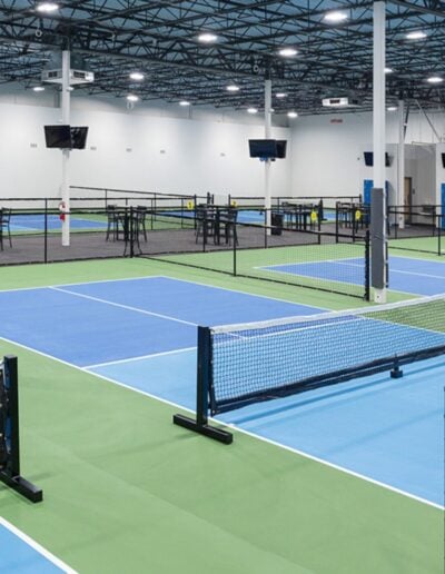 Indoor pickleball and tennis courts with vibrant blue and green surfaces, featuring nets and surrounding seating areas, designed for competitive and recreational play by Sport Pro Surfacing.