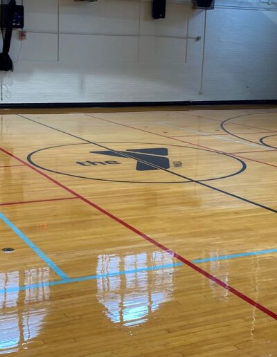YMCA basketball court with polished hardwood flooring, featuring the YMCA logo at the center and marked lines for play.