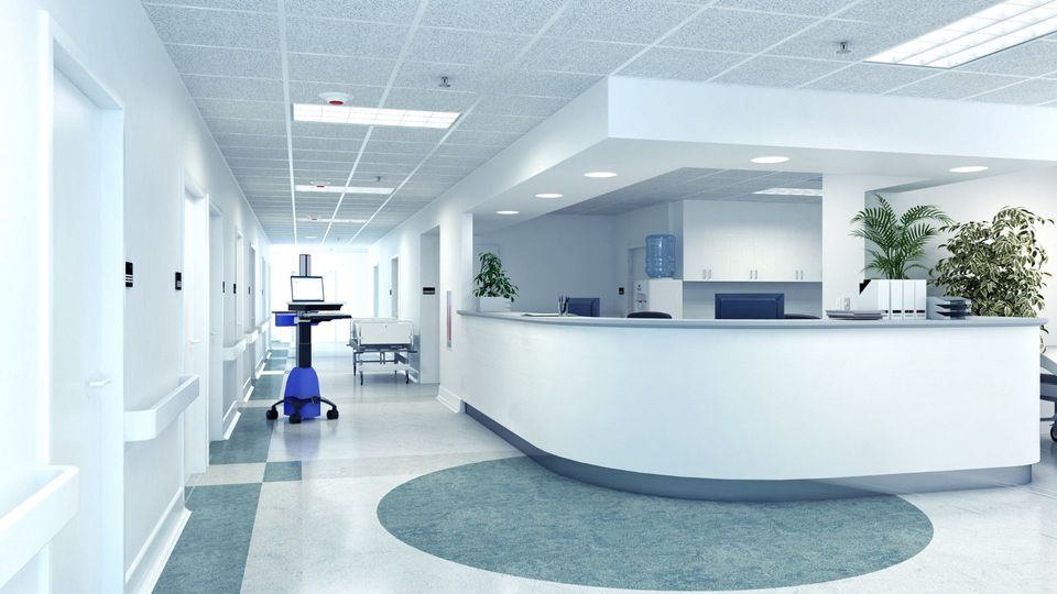Hospital rehabilitation area with modern flooring, reception desk, medical equipment, and greenery, emphasizing safety and comfort in healthcare environments.