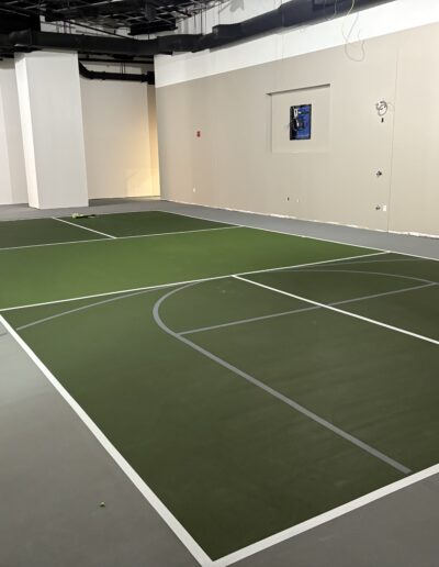 Indoor sports court surface featuring green and gray areas, marked for tennis and pickleball, showcasing professional-grade design by Sport Pro Surfacing.