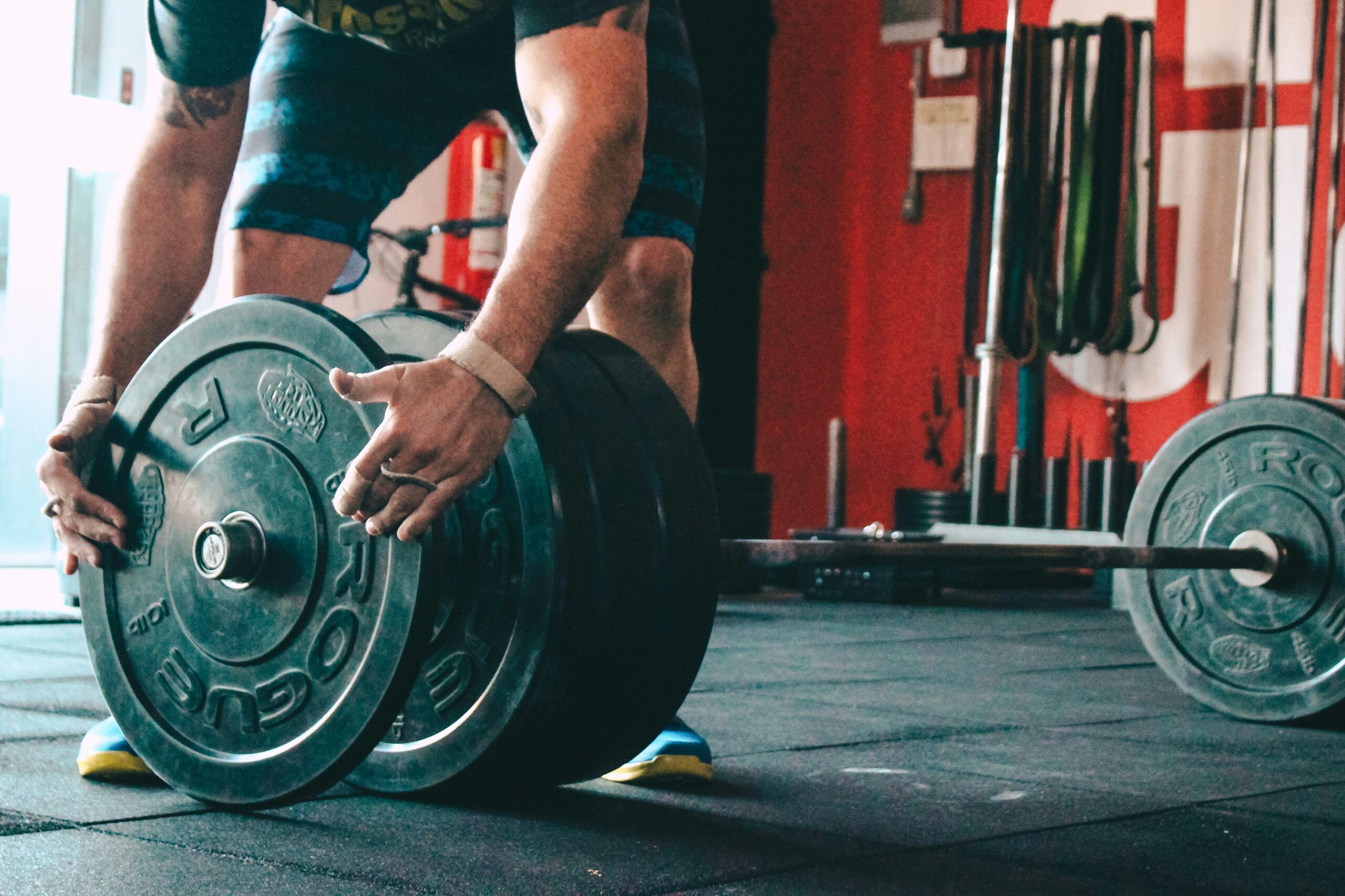 photo-1517964603305-11c0f6f66012.jpeg Person preparing to lift a barbell with weight plates on soundproof flooring in a gym setting, emphasizing noise control and safety for high-energy activities.