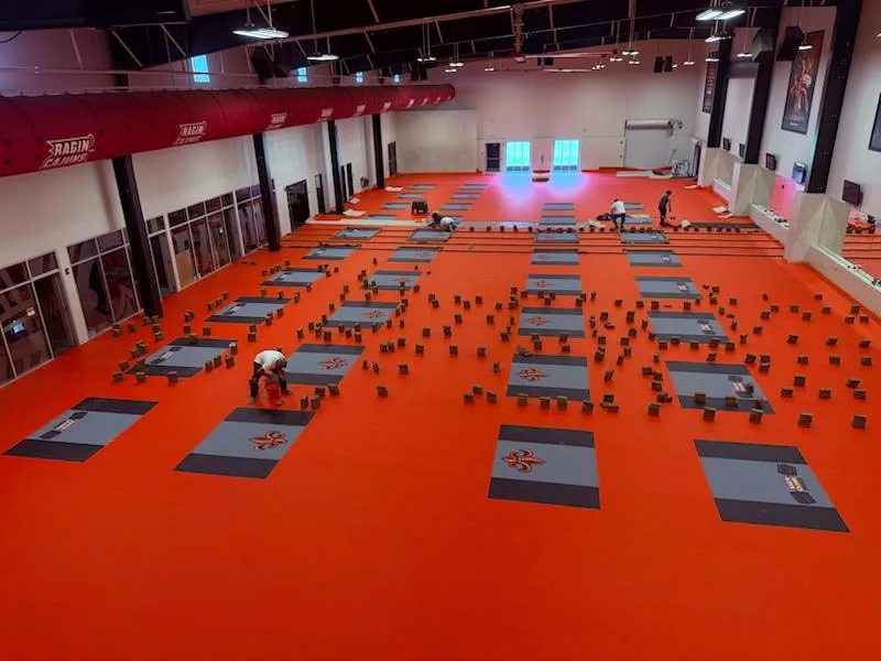 Large fitness area with orange rubber flooring and interlocking rubber mats being installed, showcasing seamless coverage for gym activities.