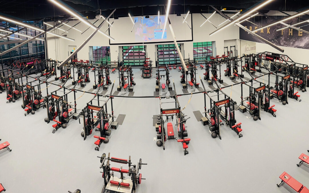 Weight room interior featuring multiple weightlifting stations, impact-resistant flooring, and modern training equipment, emphasizing athletic performance and safety.